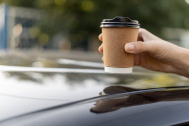Bir kadının elinin, tek kullanımlık bardağı bir arabanın çatısına koyarkenki görüntüsü. Boşluğu kopyala