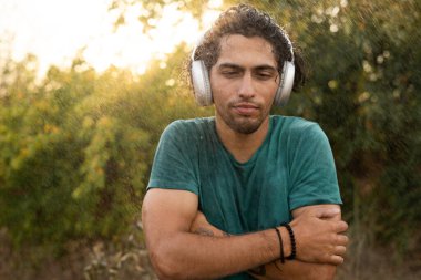 Parktaki yağmur sırasında kameraya kulaklık takan üzgün genç bir Arap. Mutsuz erkek yağmur yağarken dışarıda üşür. Adam yağmurlu havadan nefret ediyor. Boşluğu kopyala