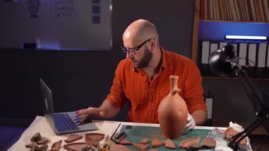 Erkek arkeolog gece geç saatlerde bir dizüstü bilgisayar kullanarak kazılarda bulunan bulgular hakkında bilgi arıyor. Boşluğu kopyala