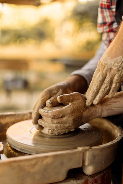 Potter teaching a woman how to work with clay on a potter's wheel, making pottery. Top view. Close-up of hands. Side view