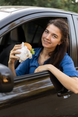 Kadın hamburger yerken araba kullanıyor ve yemek yiyor. Trafik sıkışıklığında bekleyip duruyorum. Boşluğu kopyala