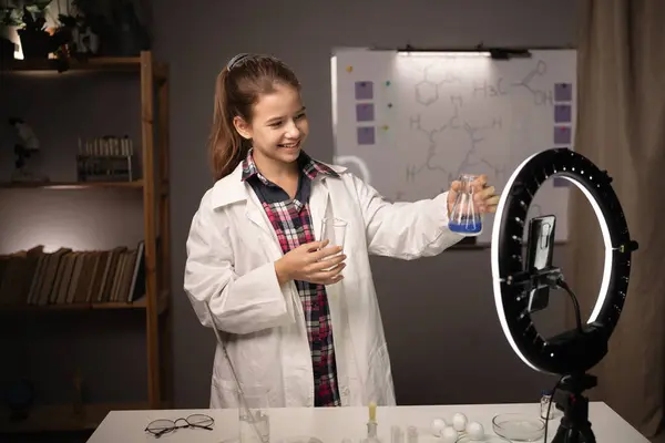 Student in lab coat making chemistry experiments at home and recording video for her followers. Child blogger. Copy space