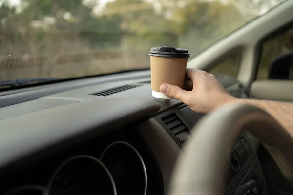 Male driver puts a glass of takeaway coffee on the dashboard in his car, close-up of his hand. Copy space
