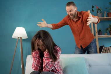 Aile kavgası. Üzgün bir eş koltukta oturuyor, kızgın koca bağırıyor, el kol hareketi yapıyor, karısını aldattığı için kıskanıyor..