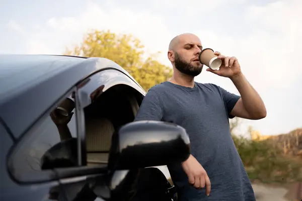 Bald man drinks coffee near the car while stopping for lunch. Copy space