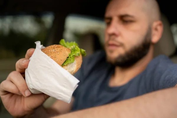 Bearded man eating hamburger in his car while driving. copy space