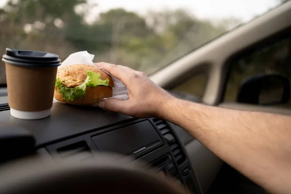 man\'s hand with hamburger and coffee in car, fast food concept. Copy space