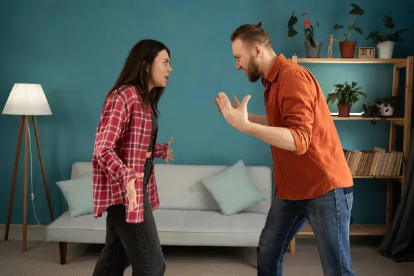Young couple arguing and fighting at home. Domestic violence and emotional abuse scene of woman and man screaming at each other in the living room. Copy space