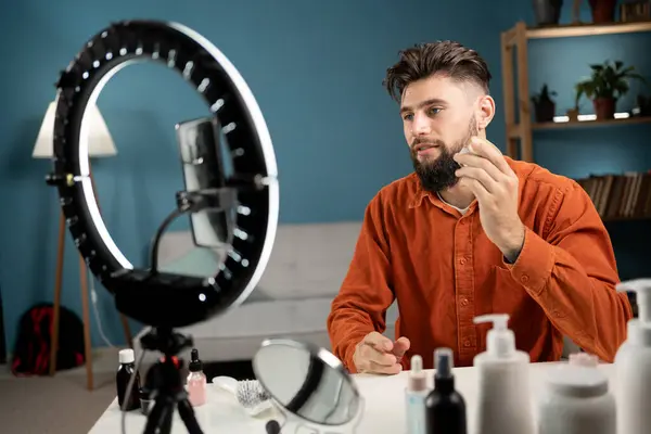 Blogger bearded man with review cosmetics product talking to camera live recording video on social network at home. Online selling cosmetics on social media. Copy space