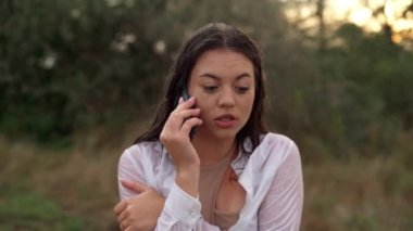 Soğuk yağmurda giysiler içinde dikilen genç bir kadının yakın plan portresi, tamamen sessiz. Akıllı telefon kullanarak bir arama yapar. Öfke duygusu. Soğuktan korkaksın. dikey video.