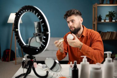 Kozmetik ürünlerini inceleyen blogcu adam evdeki sosyal ağda kameradan canlı yayın yapıyor. Kozmetik satan ve sosyal medyada canlı yayın yapan çevrimiçi tüccarlar