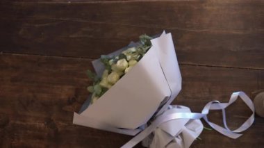 Kadın çiçekçi bir buket gülü hediye kağıdıyla paketliyor ve kurdele ile süslüyor. Üst görünüm