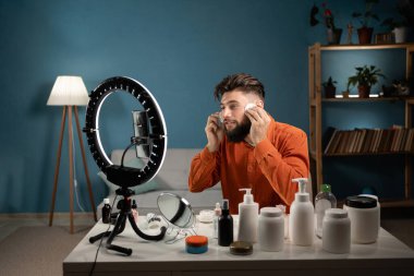 Erkek güzellik blogcusu akıllı telefon setinde yüz temizleme ve cilt bakımı ürünleri reklamını gösteren bir video hazırlıyor. Blogculuk kariyeri