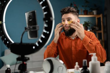 Erkek güzellik blogcusu, takipçilerle yapılan akıllı telefon konuşmalarının kamerasında kozmetik video bloğu çekiyor. Kolajen yamaları, video yayınları uyguluyor. Boşluğu kopyala