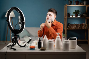 Erkek blogcu, cilt rutiniyle ilgili güzellik blogu için özel ders videosu kaydediyor. Vlogger yüz maskesi takıyor, sosyal ağ için video kaydediyor. Günlük konsepti