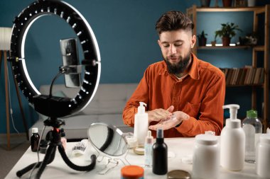 Akıllı telefondan video çeken adam, nüfuzlu blogger sosyal ağ için güzellik blogu kaydediyor, evde kozmetik ürünleri gösteriyor. Boşluğu kopyala