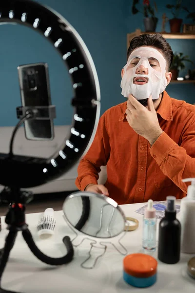 Male blogger recording tutorial video for his beauty blog about skincare routine. Vlogger applying face mask, recording video for social network. Blogging concept