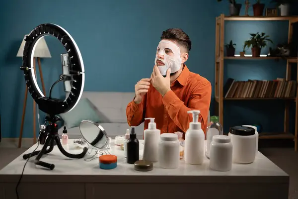 Male blogger recording tutorial video for his beauty blog about skincare routine. Vlogger applying face mask, recording video for social network. Blogging concept