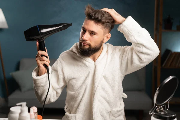 Hair care and grooming concept. Man uses hairdryer, going to make hairstyle after taking shower, drying hair. Copy space