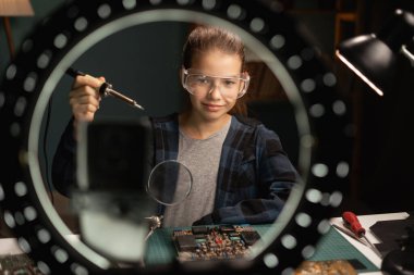 Yüzük ışığı ve akıllı telefonlu mutlu gülen kız blogcu evde lehimlemekten bahsediyor. Bloglama, teknoloji ve hobi kavramı