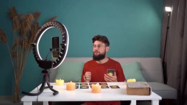 Profesyonel internet flaması Tarot kartları kullanarak fal bakar. Video yayını için akıllı telefonu ve halka lambasını kullanarak canlı yayın. Kameranın önüne geçer, kartları karıştırır ve düzenler..