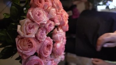 Mağazadaki vazolardan buket pembe güller toplayan kadın çiçekçi. Dikey video
