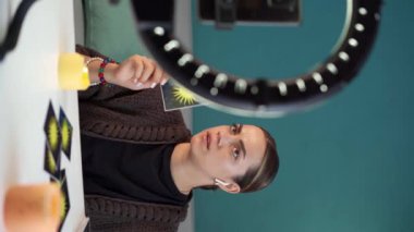 Sosyal ağlar için video blogu kaydederken internette tarot falına bakan genç bir kadın. Kartı müşteriye kamerada gösterir. Dikey video