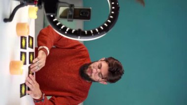 Vlogger, blogger falcısı takipçileri için cep telefonuyla canlı yayın tahmini geleceği kullanıyor evde tarot kartları çevrimiçi. Dikey video