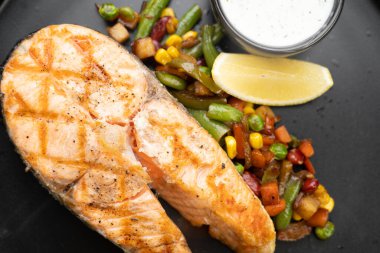 Siyah ahşap masada sebzeli kızarmış somon bifteği. Yakın plan.