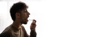 İlaç ve tedavi kavramı. Arap adam boğaz spreyi kullanıyor, beyaz şişeyi ilaçla tutuyor. Beyaz arka planda. Boşluğu kopyala