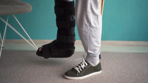 受伤的男人腿上有黑色的夹板 在家里走着拐杖 脚踝足部矫形 复制空间 — 图库视频影像