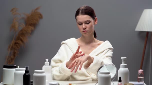 穿着白色浴衣的年轻女人在手上涂母乳 在卧室里给皮肤保湿 复制空间 — 图库视频影像