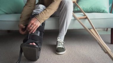 Genç adam ciddi bir yaralanmadan sonra evdeki kanepede otururken bileklik takar. Boşluğu kopyala
