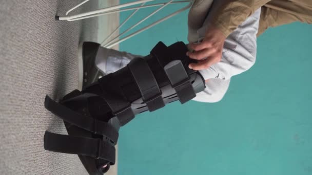 Чоловік Кладе Пішохідну Дужку Ногу Сидячи Дивані Вдома Ортез Щиколотки — стокове відео