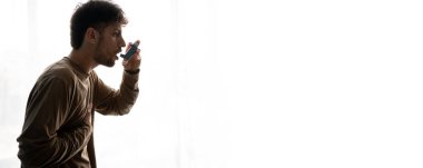 Beyaz arka planda duran bir adam saldırıda astım spreyi kullanıyor. Alerjilerle savaş, astım. Pankart. Boşluğu kopyala