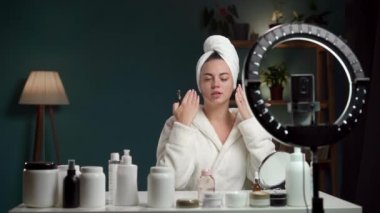 Havlu ve bornozlu kadın blogcu, video kaydederken ve güzellik blogu için tavsiye verirken güzel cilt için yüz silindiri gösteriyor. Boşluğu kopyala