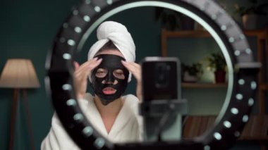 Kadın blogcu etkileyicisi abonelerle video iletişimini kaydediyor, cilt ürününden bahsediyor, duştan sonra cildine siyah yüz maskesi takıyor. Boşluğu kopyala