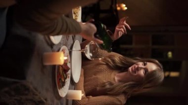 Genç ve tutkulu bir çift evde mum ve kırmızı şarapla romantik bir akşam yemeği yiyor, adam bardaklara şarap dolduruyor. Dikey video