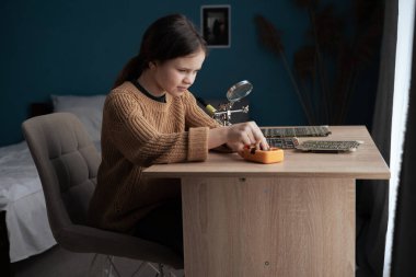 Eğitim Konsepti. Akıllı liseli kız evde elektronik ve lehim telleri ve devre kartlarını inceliyor. Boşluğu kopyala