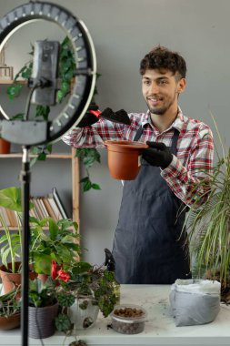 Arap genç adam sosyal medya kanalı blogcusu ev bahçesi, bahar bitkisi bakımı ve bitki nakli dersleri hakkında video kamerayla video blogu kaydediyor, çiçek saksısı drenajını gösteriyor. Boşluğu kopyala