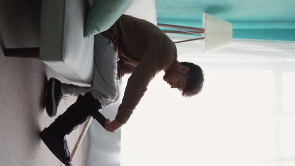 男人把脚踝支架放在腿上 坐在沙发上 在家里用拐杖 垂直录像 — 图库视频影像
