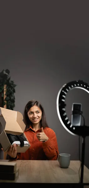 Woman unboxing parcel with VR Glasses at camera, recording video for her technology blog at home. Concept of people, technology and blogging