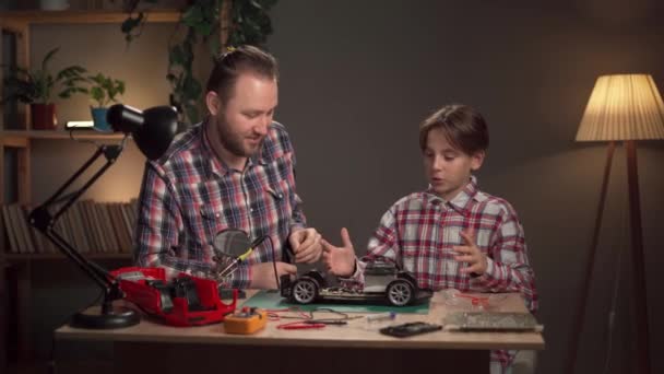 爸爸和儿子戴着防护眼镜 在家里用焊铁修理电动玩具车 家庭和关系的概念 复制空间 — 图库视频影像