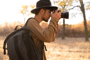 Fotoğrafçı sonbaharda ormanda günbatımında fotoğraf çekiyor. Kameralı seyahat fotoğrafçısı doğanın fotoğrafını çekiyor. Boşluğu kopyala