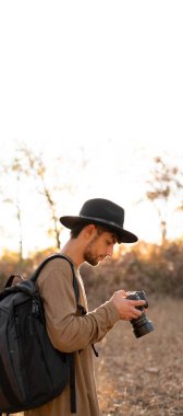Gezgin fotoğrafçı sonbaharda doğa fotoğrafı ya da dağ manzarasının videosu çekiyor. Gezgin turist profesyonel videograf DSR kamerasında macera tatili çekimi yapıyor. Uzayı kopyala Dikey pankart