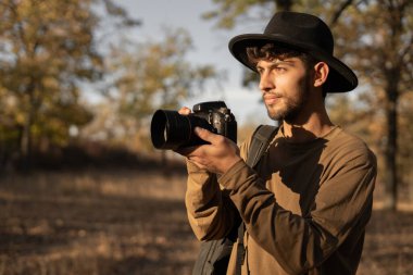 Şapkalı ve dijital kameralı seyahat fotoğrafçısının portresi gün batımında doğanın fotoğrafını çekiyor. Boşluğu kopyala