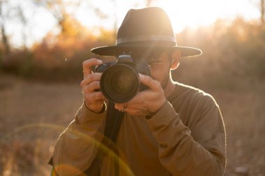 Gün batımında doğada fotoğraf çeken şapkalı fotoğrafçı portresi. Seyahat, yaşam tarzı, hobi ve macera konsepti. Boşluğu kopyala
