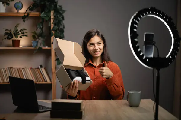Woman unboxing parcel with VR Glasses at camera, recording video for her technology blog at home. Concept of people, technology and blogging. Copy space