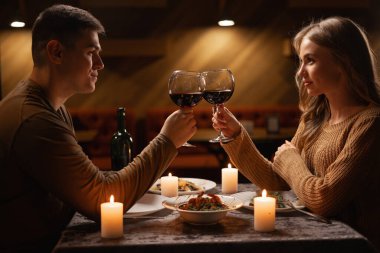 Young lovers having romantic dinner and drinking red wine at home. Celebrating Valentines Day or anniversary sitting at table at home Valentine's Day concept clipart