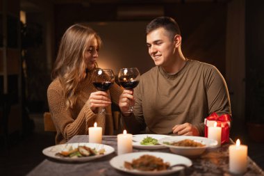 Romantik bir çift, sevgililer gününde romantik bir akşam yemeği sırasında evlerinde, sıcak bir atmosferde, kırmızı şarap kadehleriyle çıkıyorlar. Boşluğu kopyala